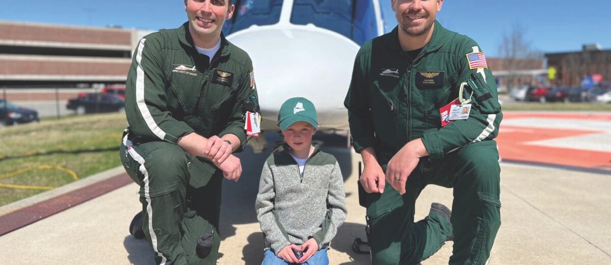 Two male LifeFlight staff and a small boy pose in front of a helicopter