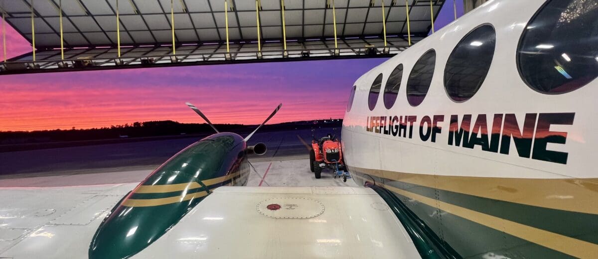 View of a pink and purple sunset from an open hangar, over the wing and fuselage of LifeFlight airplane.