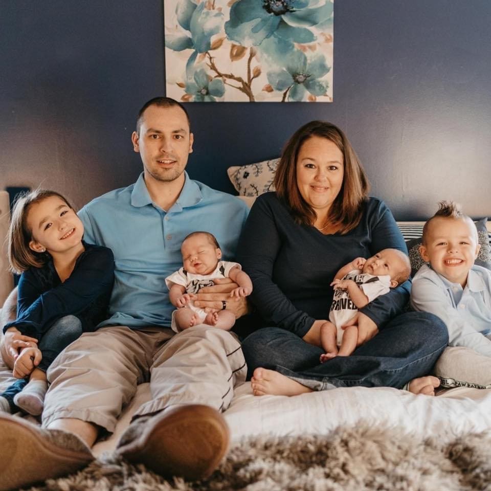 The Dolan family, daughter, father, mother, brother, and new twins, seated on a couch.