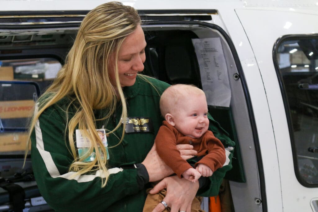 Flight Nurse Denise Saucier holds former patient Oliver White in front of a helicopter.