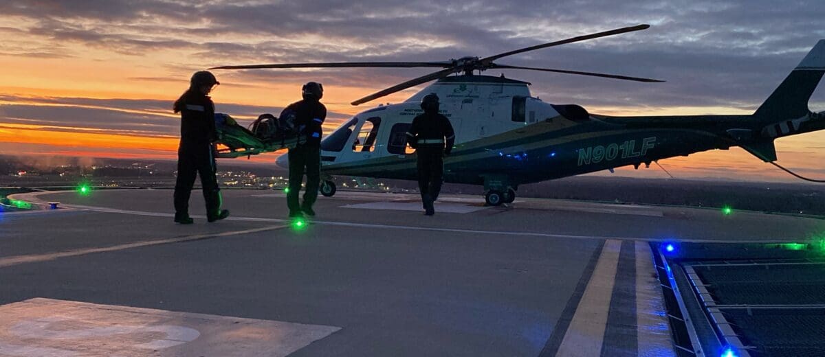 A LifeFlight crew carries an empty stretcher to the helicopter at sunset.