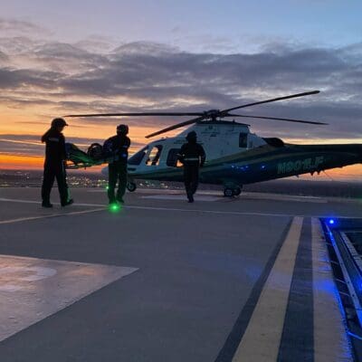 A LifeFlight crew carries an empty stretcher to the helicopter at sunset.