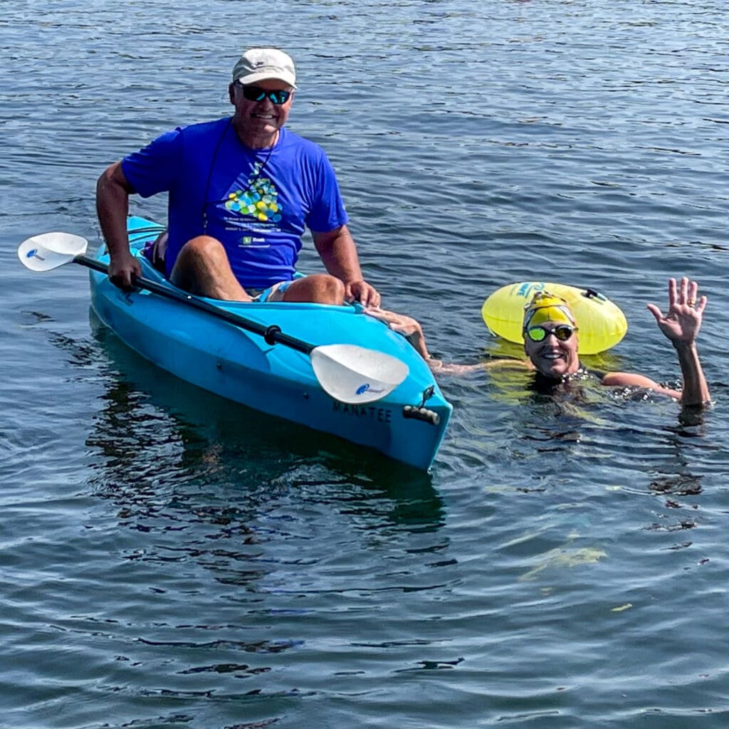 Karen Morgan swimming in a lake next to her kayaker.
